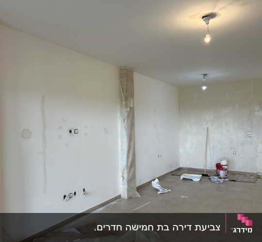 חדר בשיפוץ עם קירות מטויחים, פח צבע וכלים על הרצפה